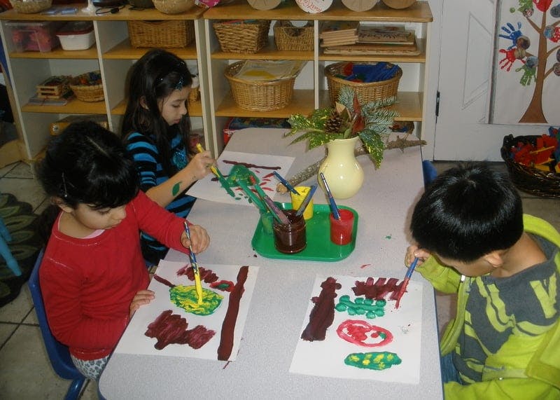 Three children painting at a table in a classroom