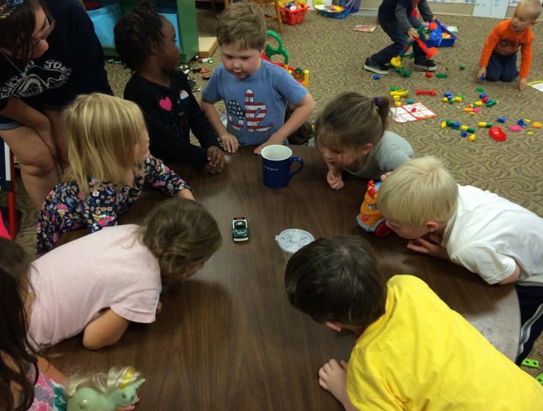 Children gathered around a table looking at a toy car