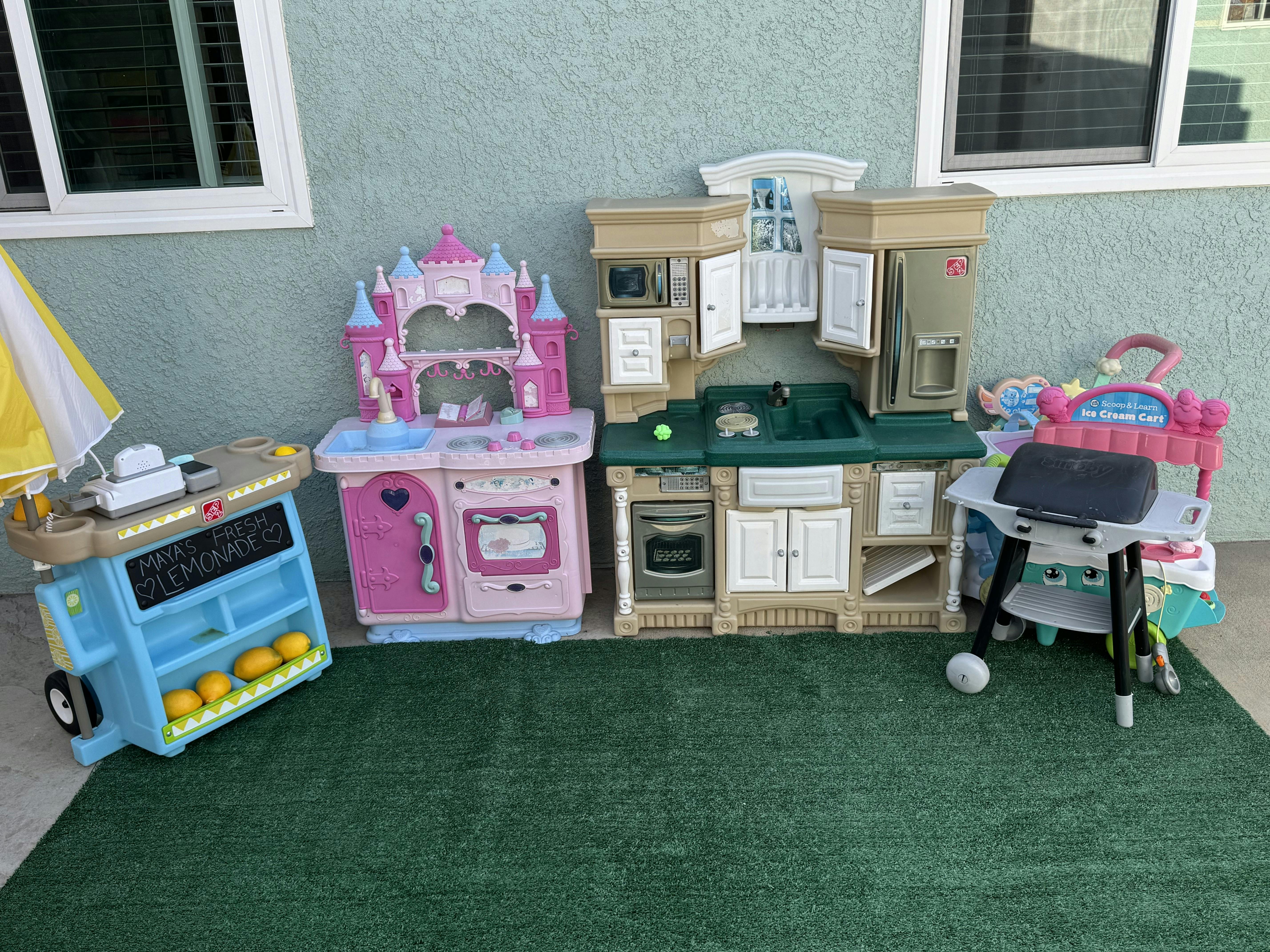 Collection of toy kitchens and a toy food stand on a green mat