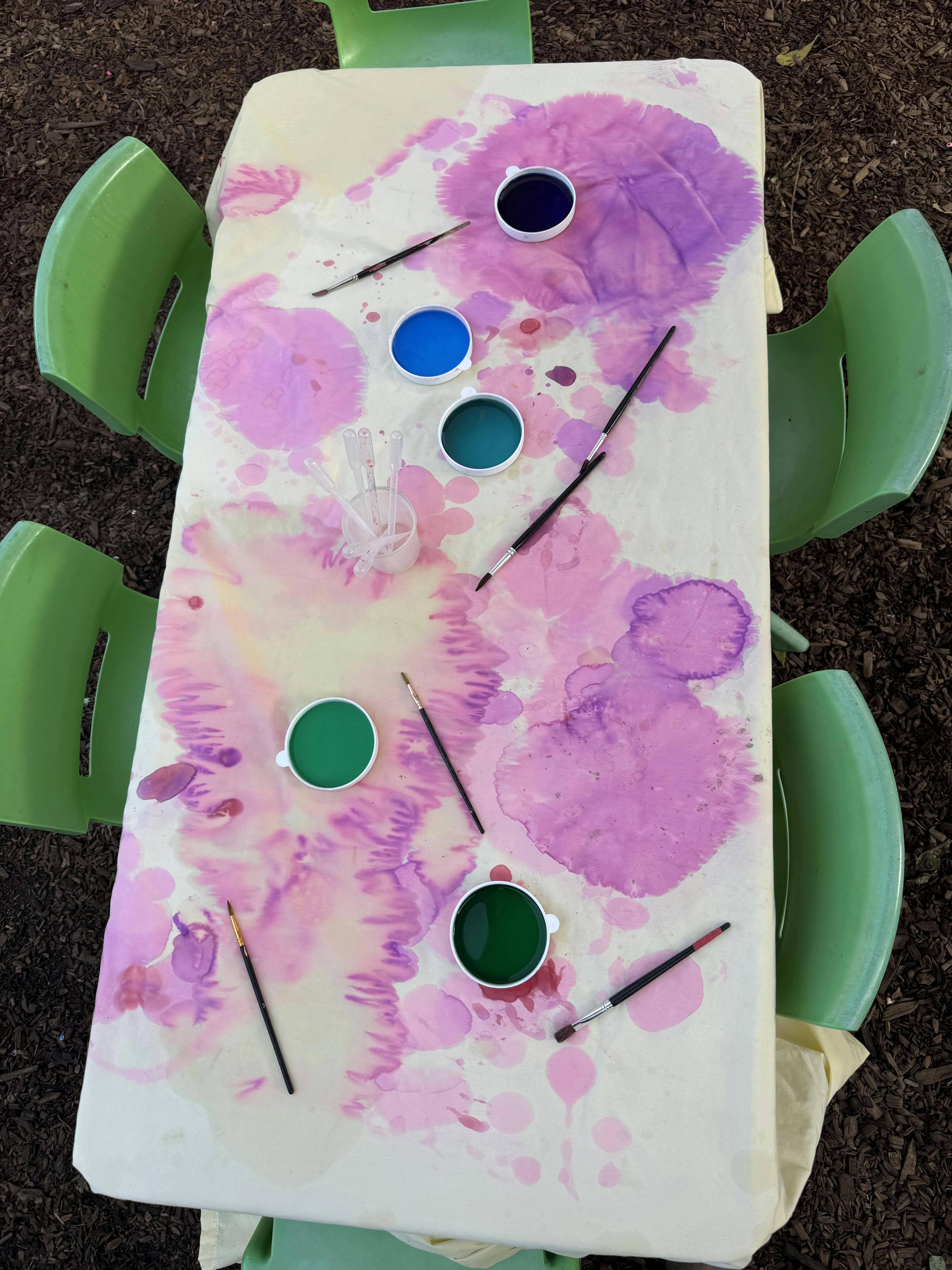 Top-down view of paint cups and brushes on a stained tablecloth
