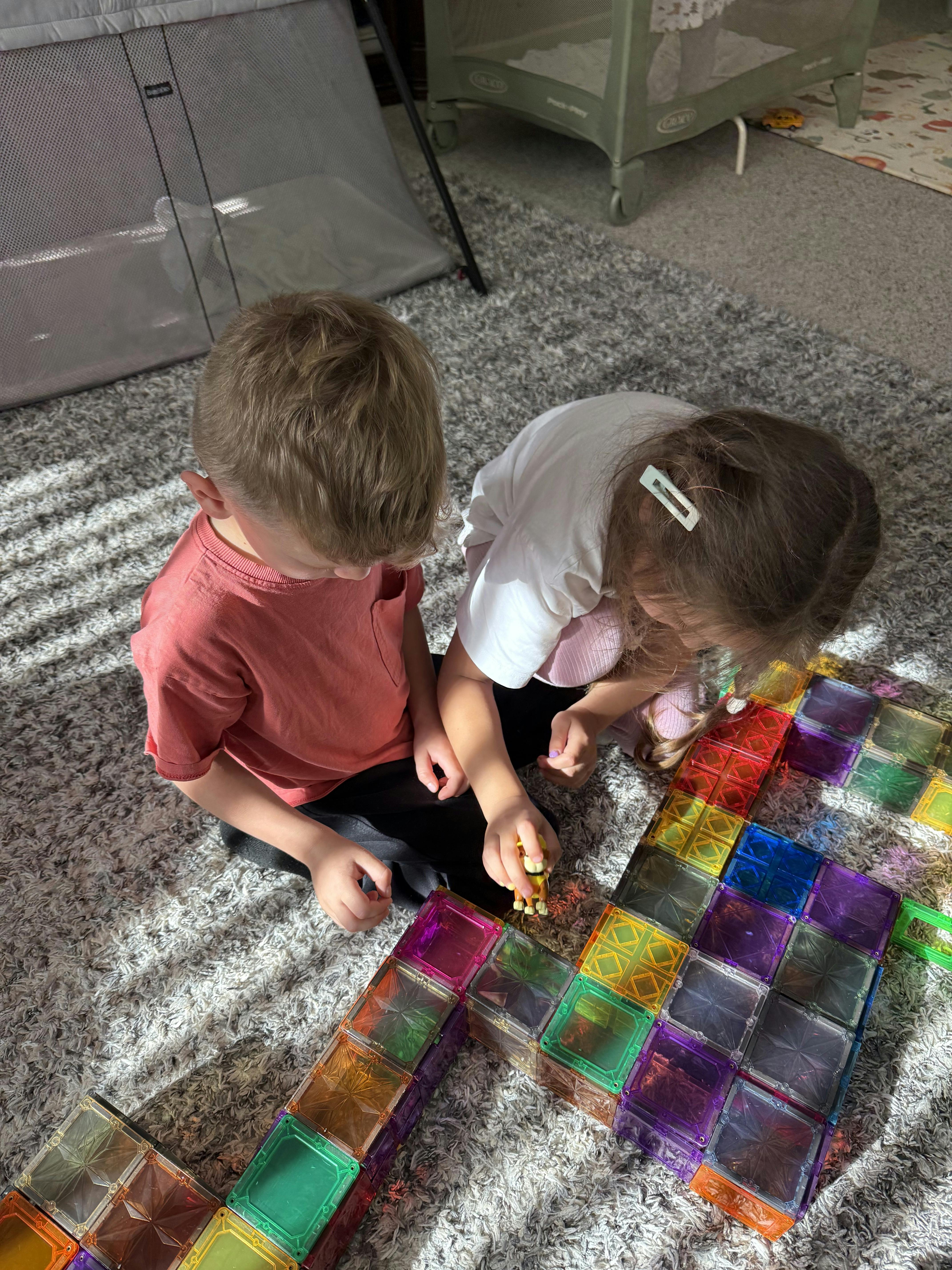 Two children playing with colorful magnetic building tiles on a rug