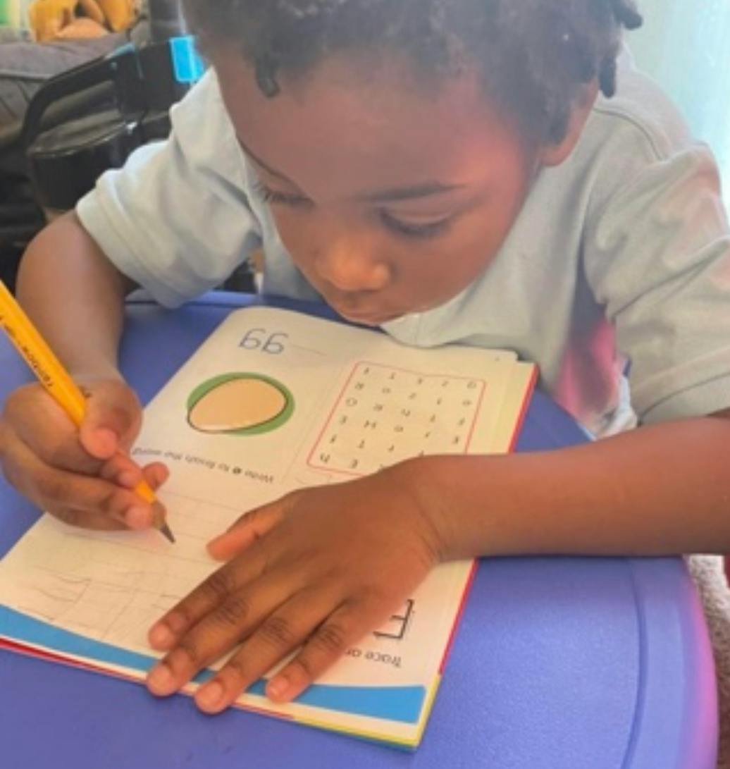 Child writing in a workbook with a pencil