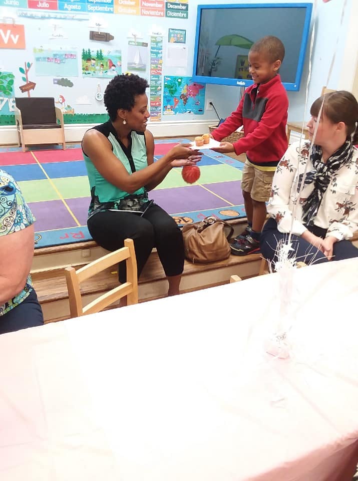 Child offering a plate of food to a person in a classroom