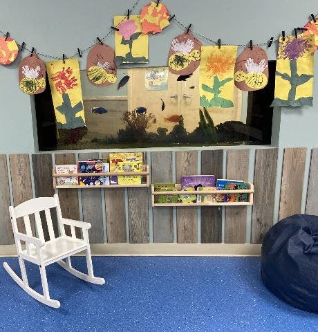 Children's artwork hanging above bookshelves, a white rocking chair, and a beanbag