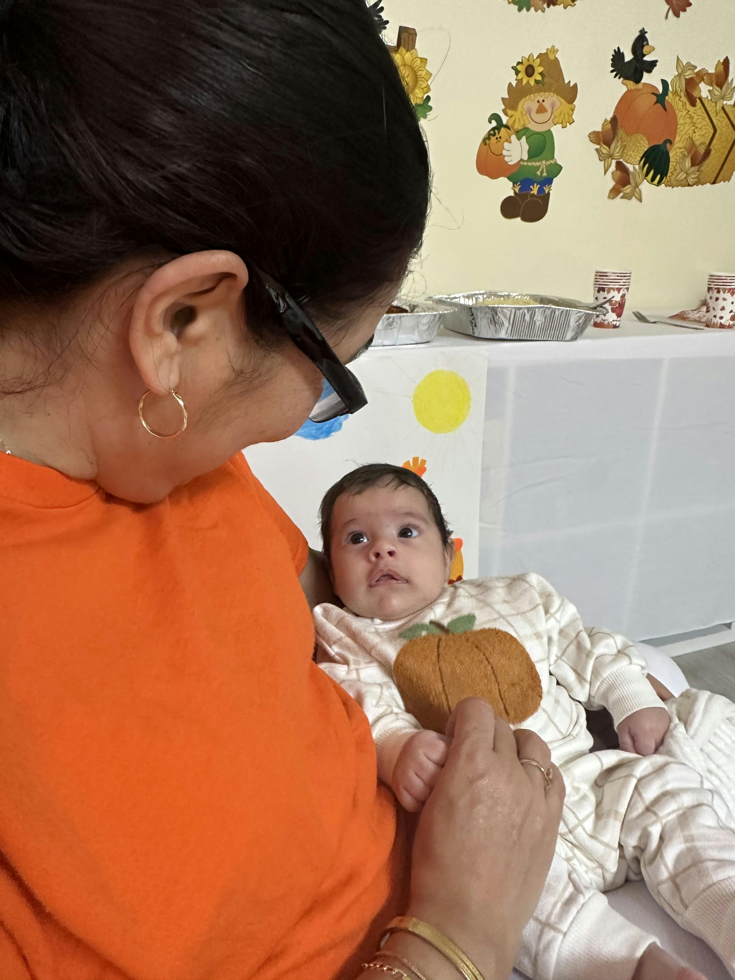 Person in orange shirt holding a child in a pumpkin-themed outfit