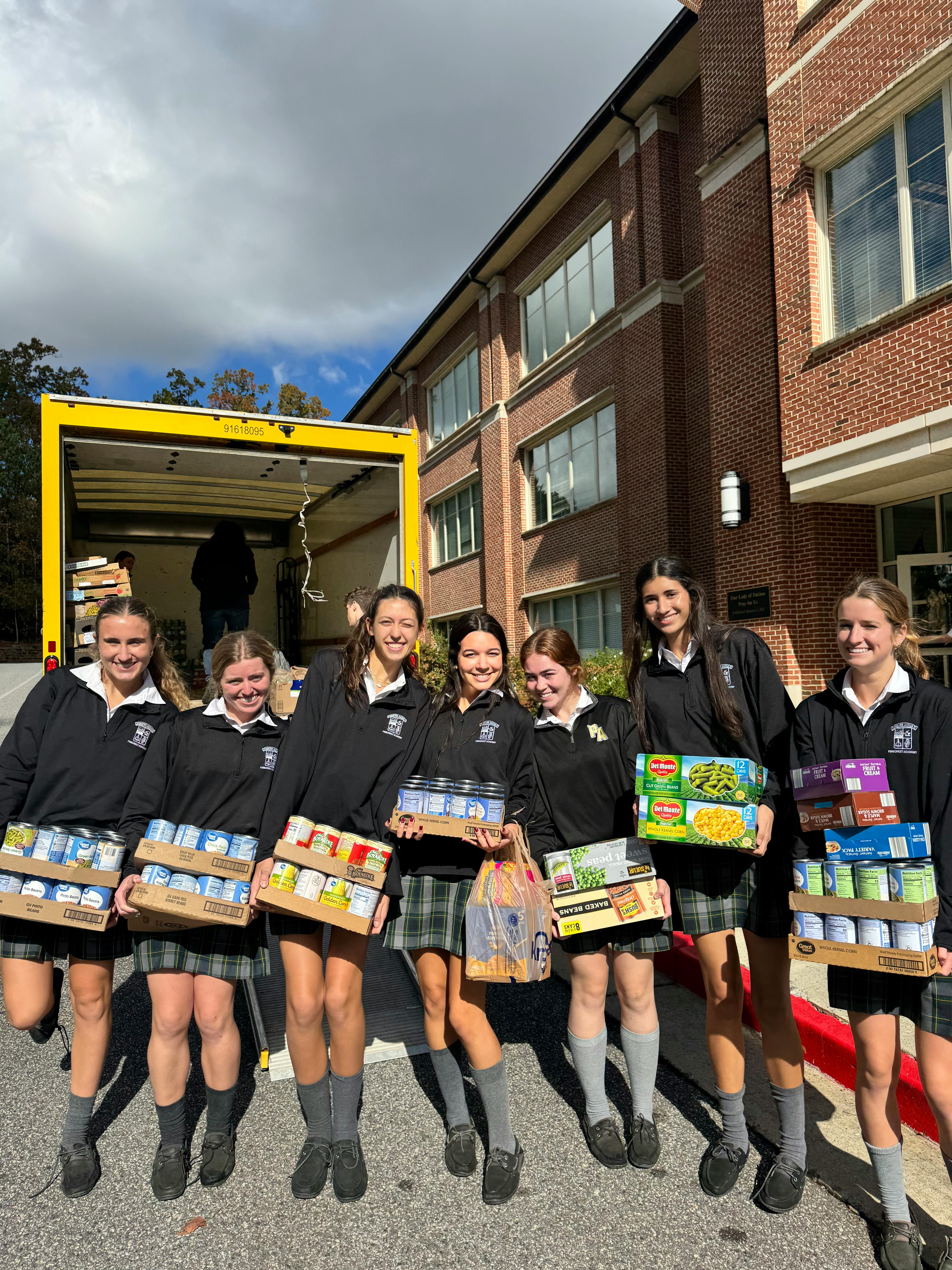 Six teens holding boxes of canned goods and groceries in front of a moving truck