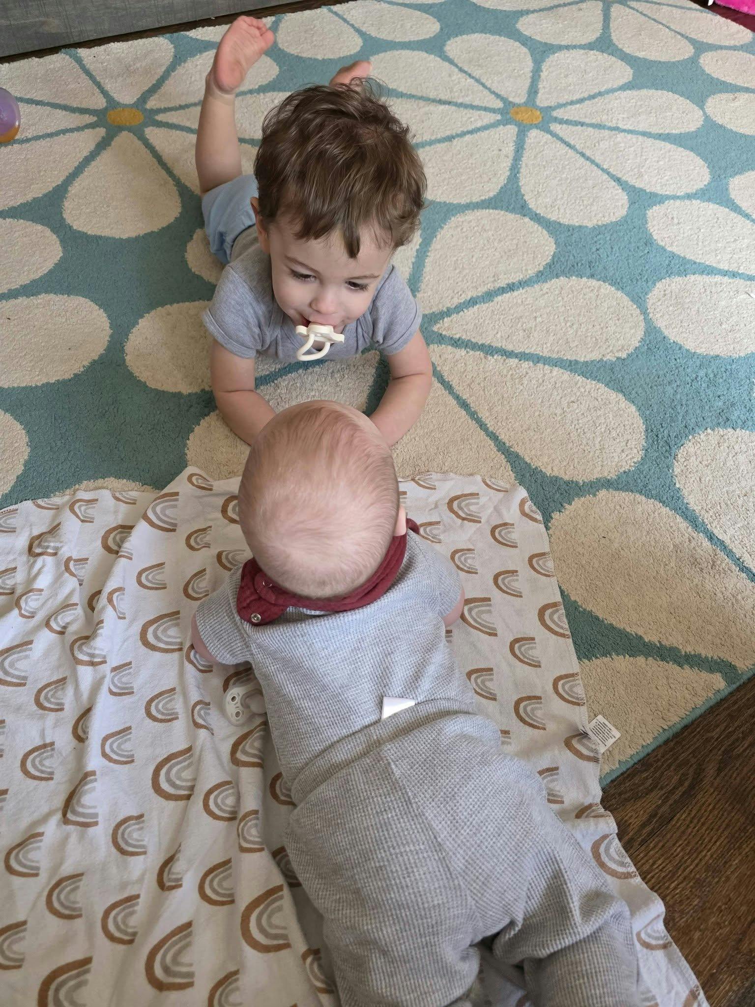 Two infants facing each other on a patterned rug and blanket