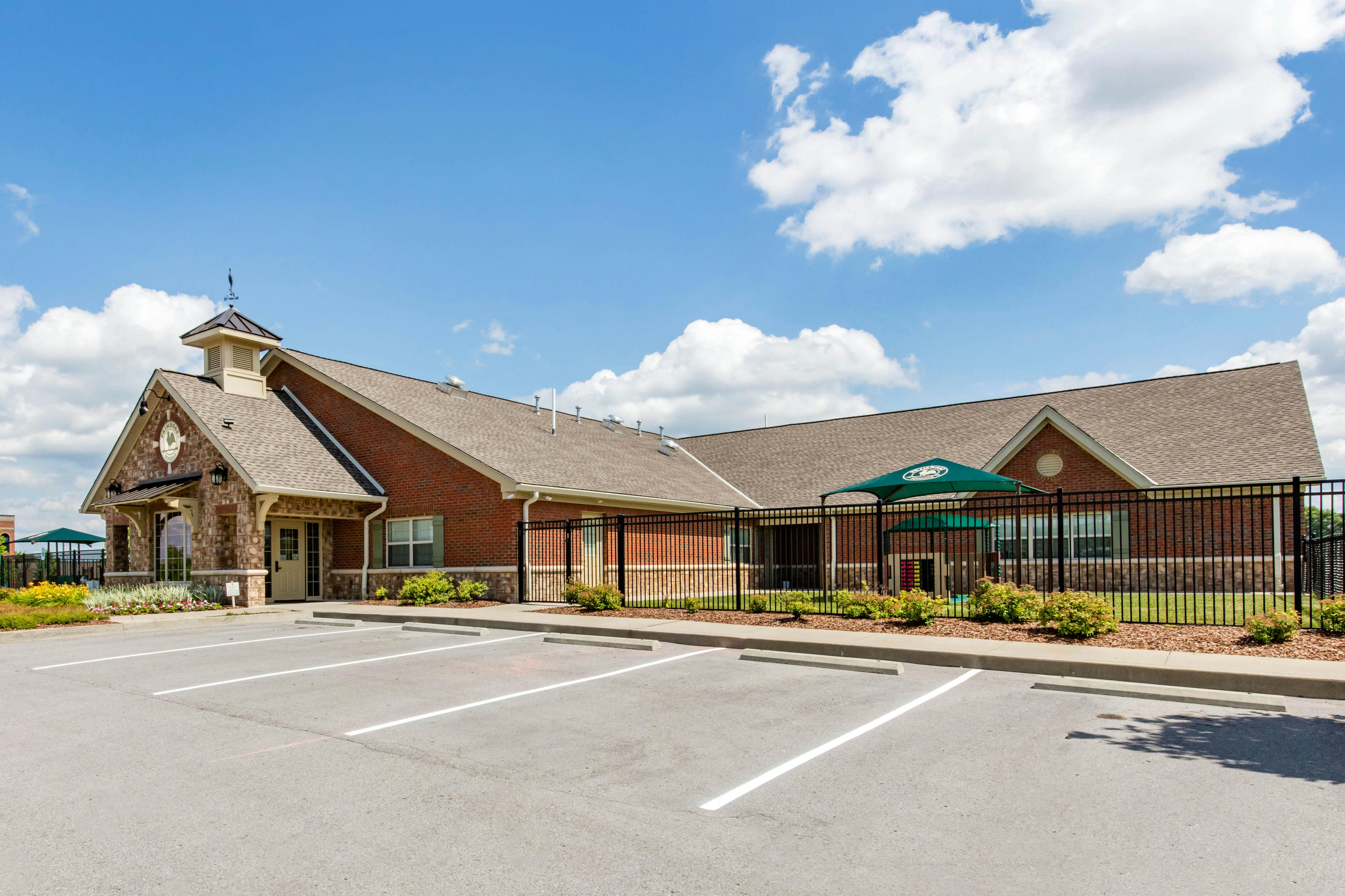 Brick building with a stone entrance, weather vane, and playground under a fence