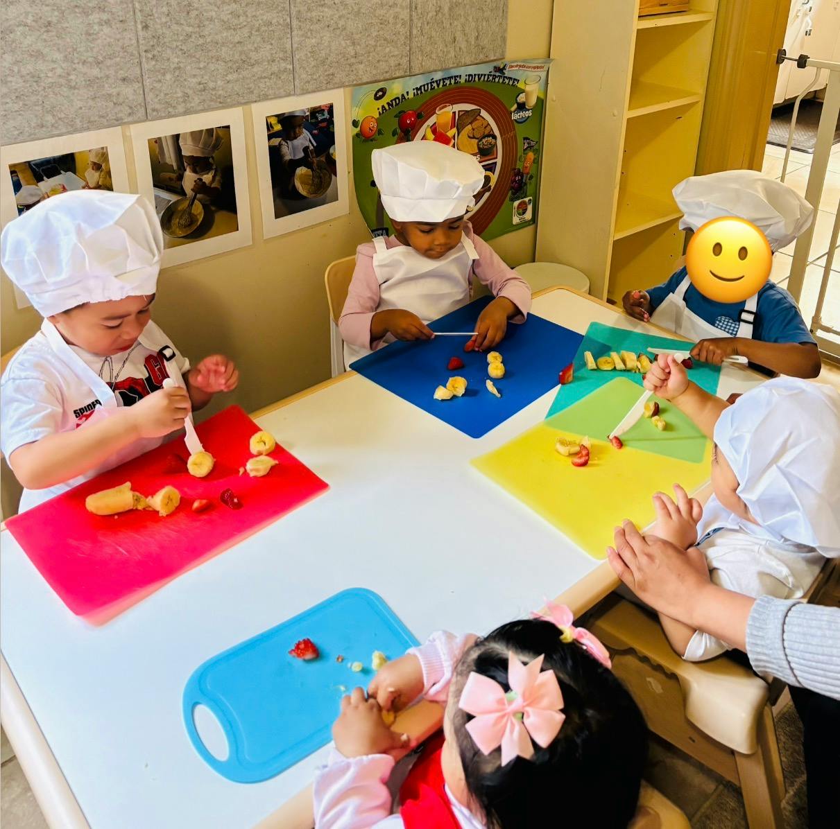 Children wearing chef hats cutting fruit on colorful mats at a table