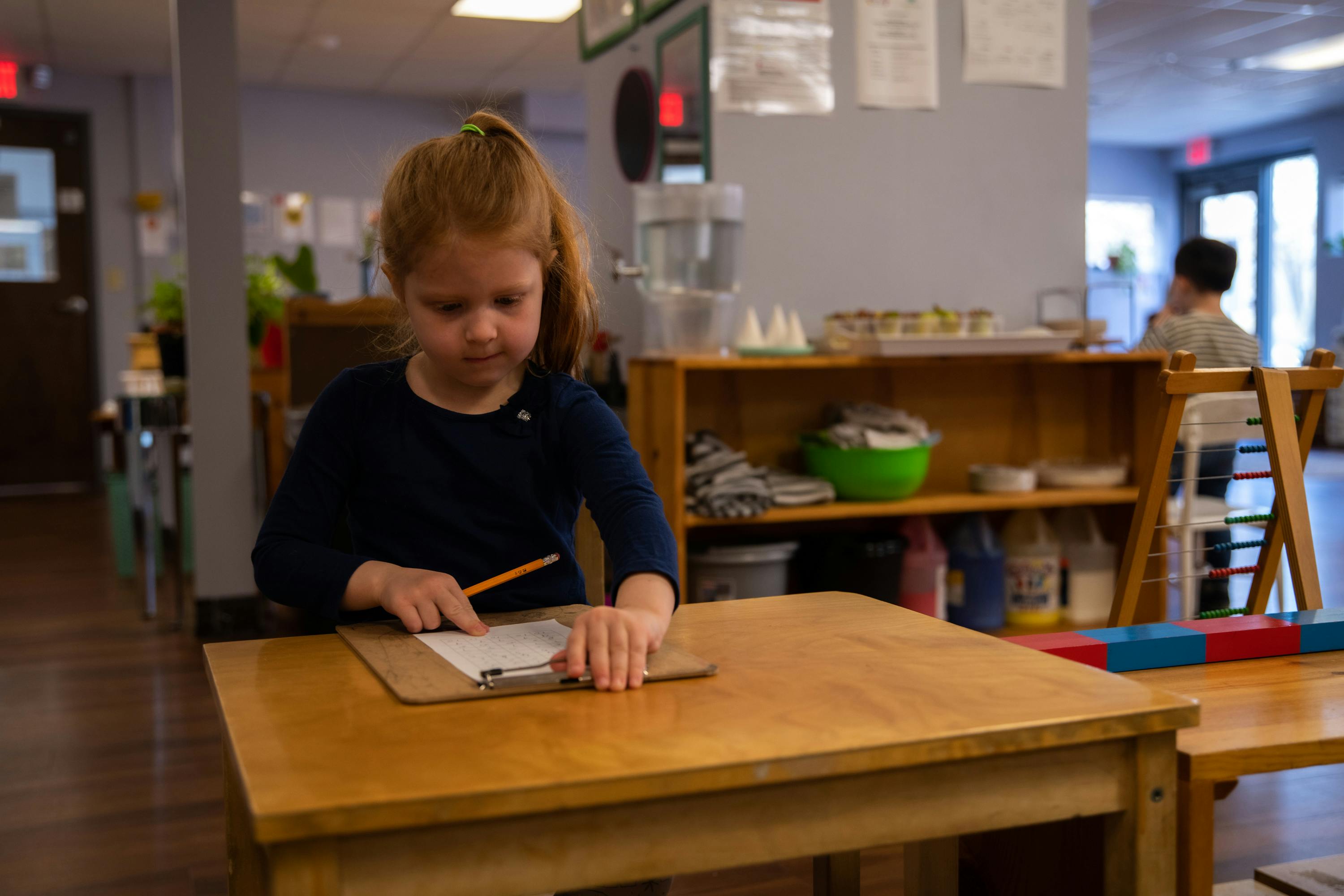 Child writing on a clipboard at a table in a classroom