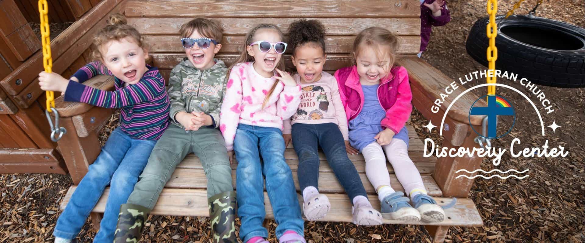 Five children sitting on a wooden swing