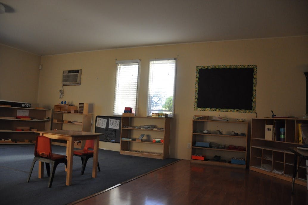 Empty classroom with small tables and chairs, shelves, and a blackboard