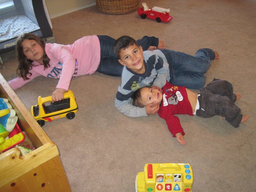Three children lying on a carpeted floor with toys