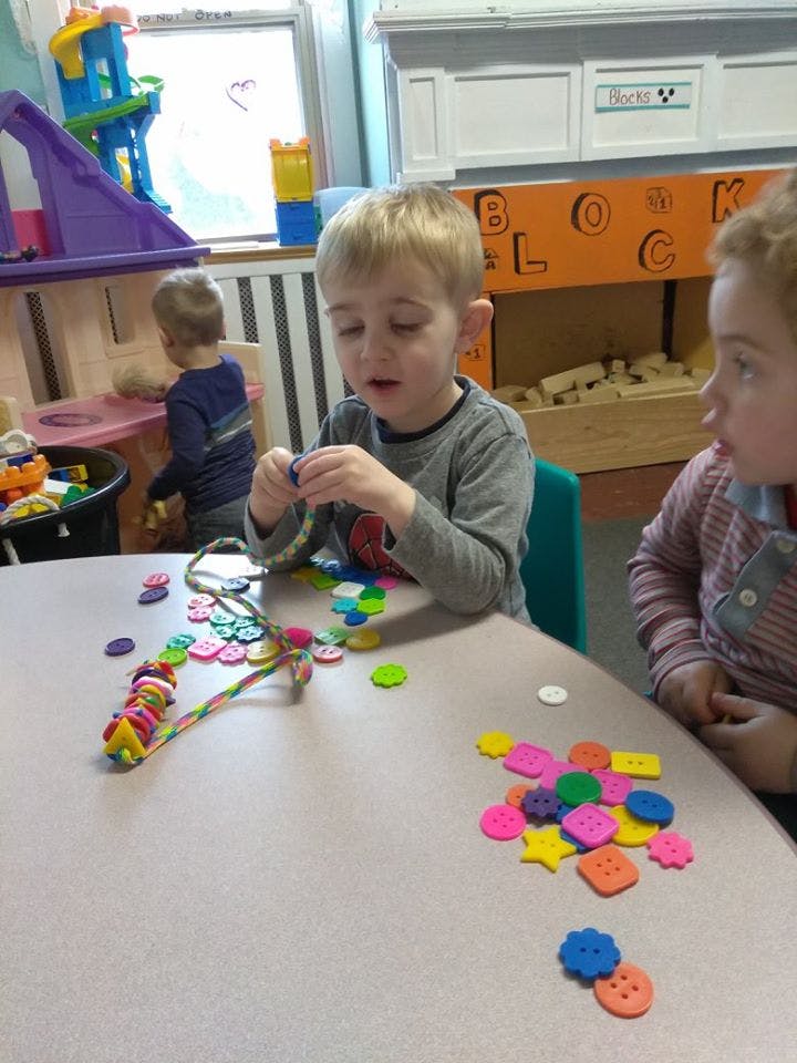 Child stringing beads at a table with another child