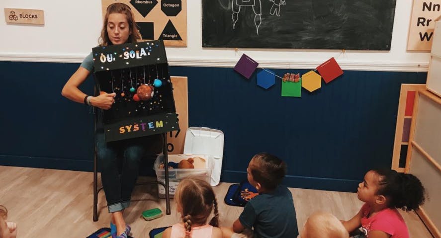 Person wearing a solar system model and speaking to children in a classroom