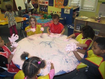 Children playing with shaving cream on a table in a classroom
