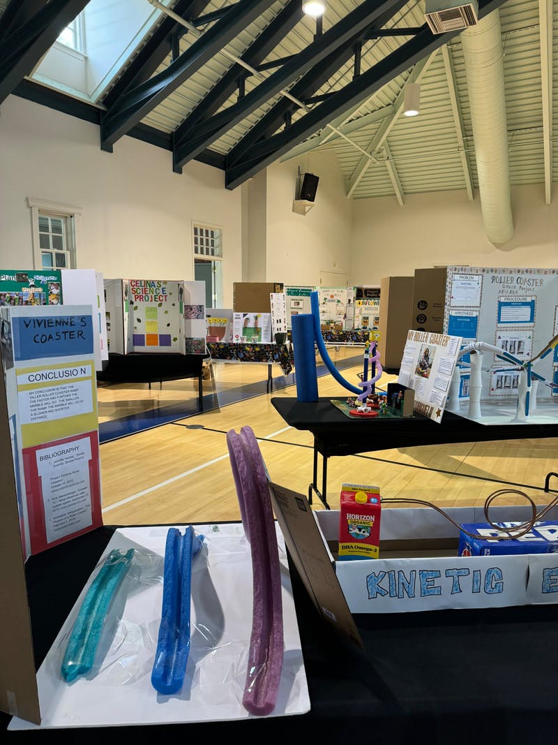 Science fair projects displayed in a gym, with various models and presentation boards