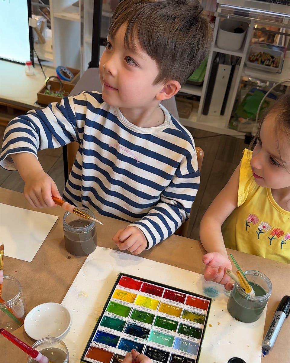 Two children painting with watercolors at a table
