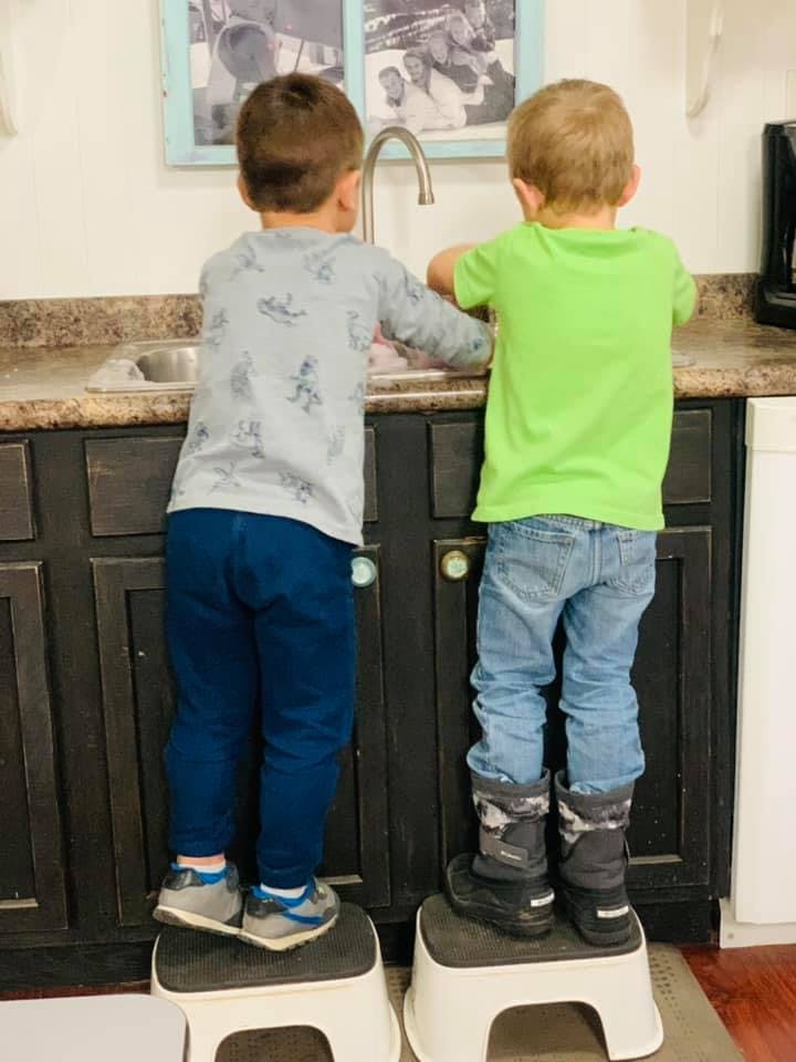 Two children standing on stools at a kitchen sink
