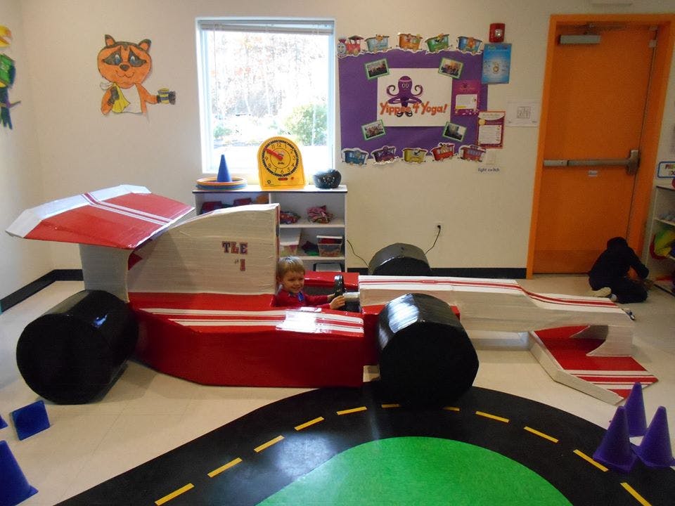 Child in a red and white race car toy in a room