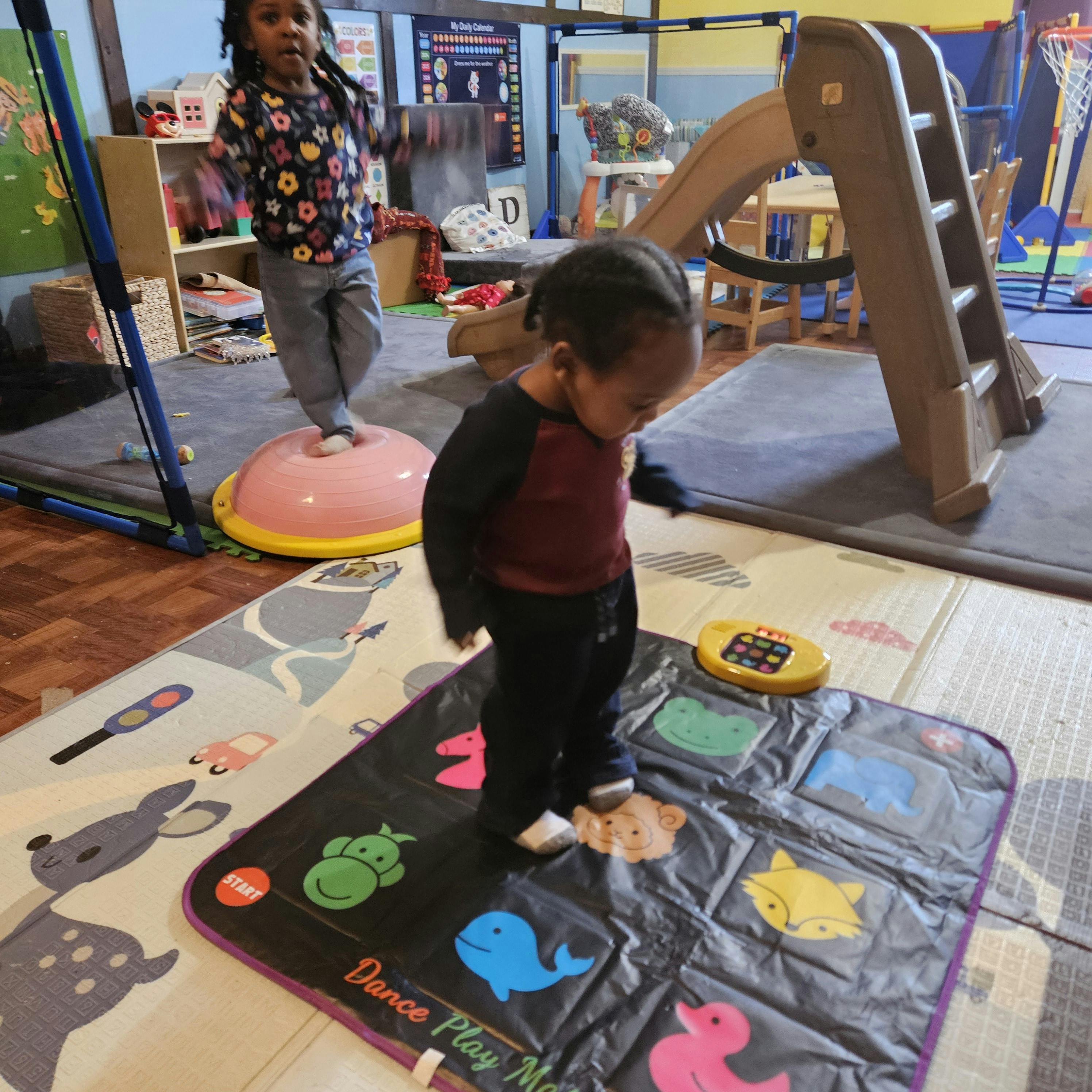 Two children playing, one on a balance dome and one on a dance mat