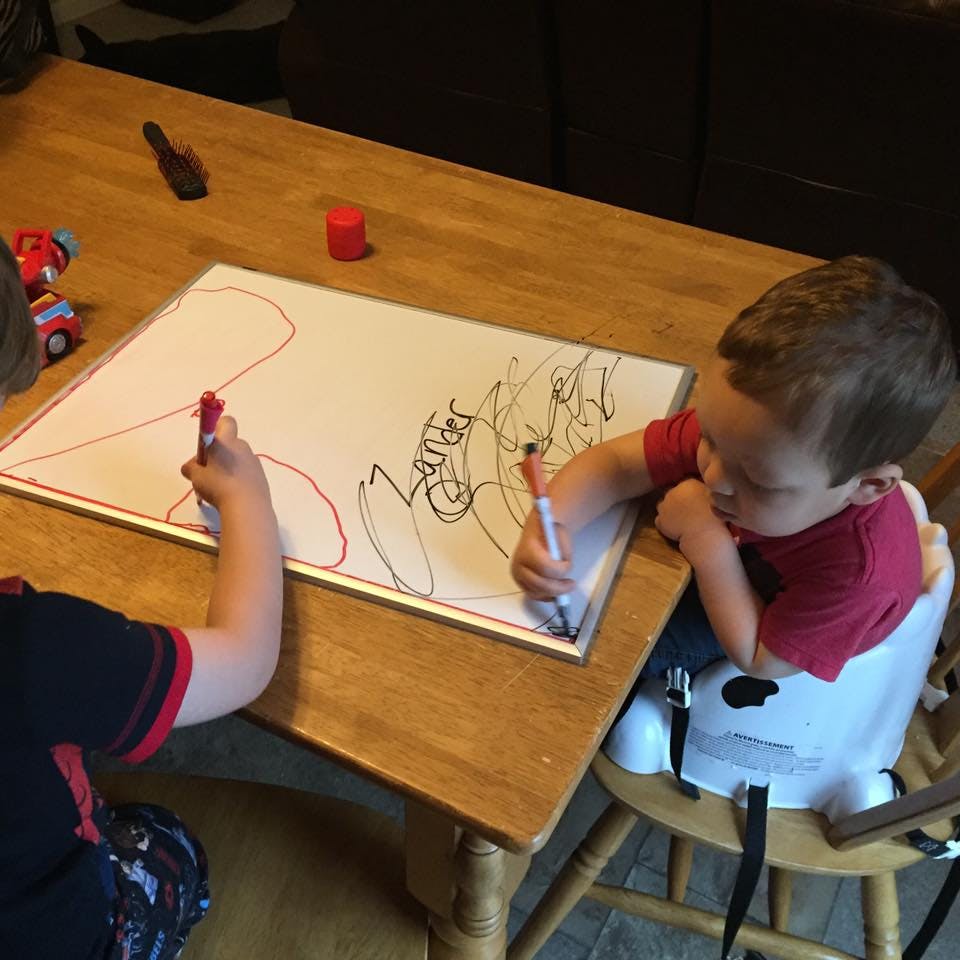 Two children drawing on a whiteboard at a table