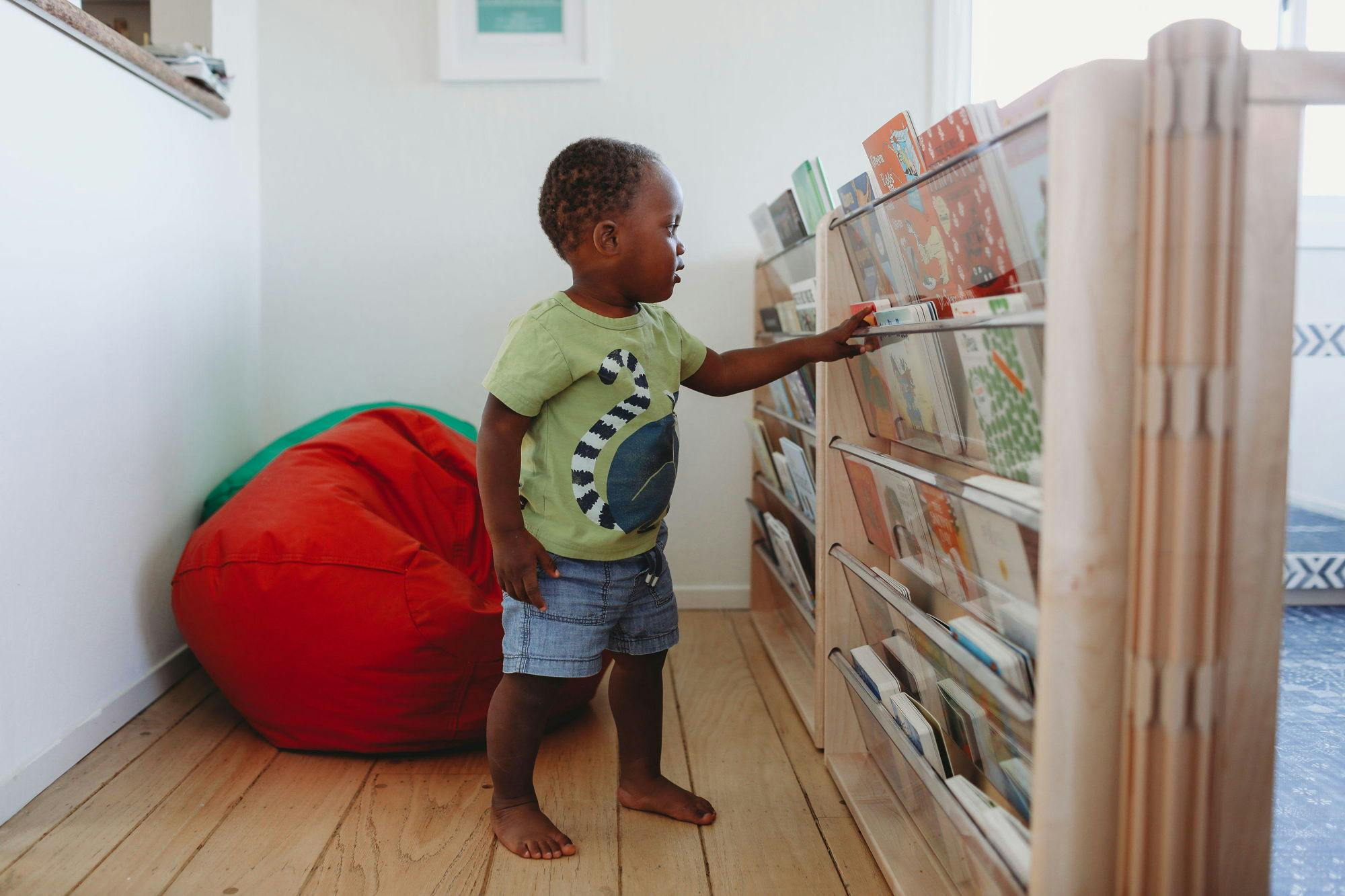 Child reaching for a book on a low bookshelf