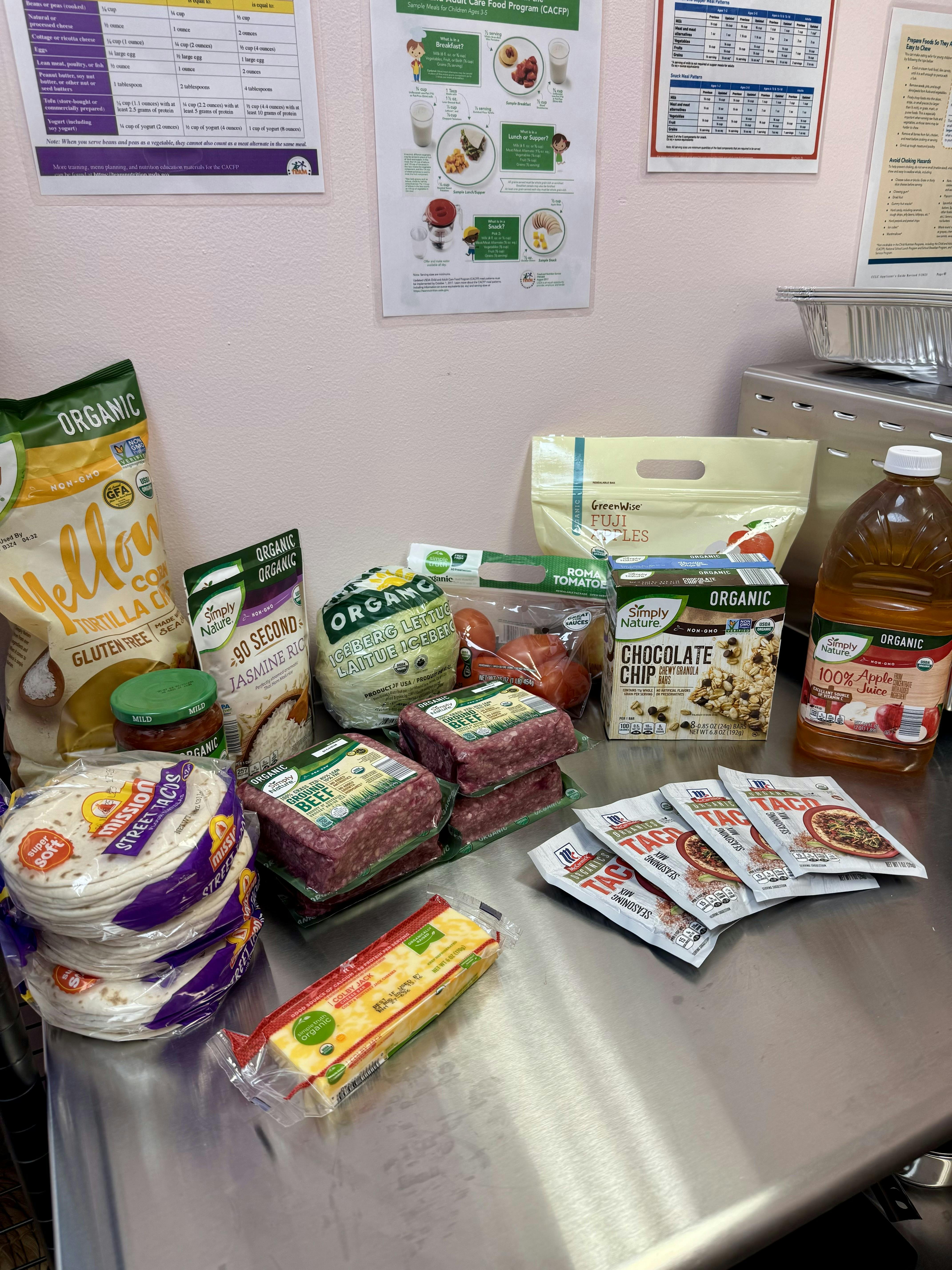 Various organic groceries including ground meat, tortillas, and juice on a metal counter