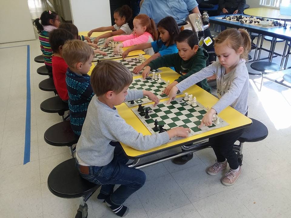 Children playing chess at individual desks