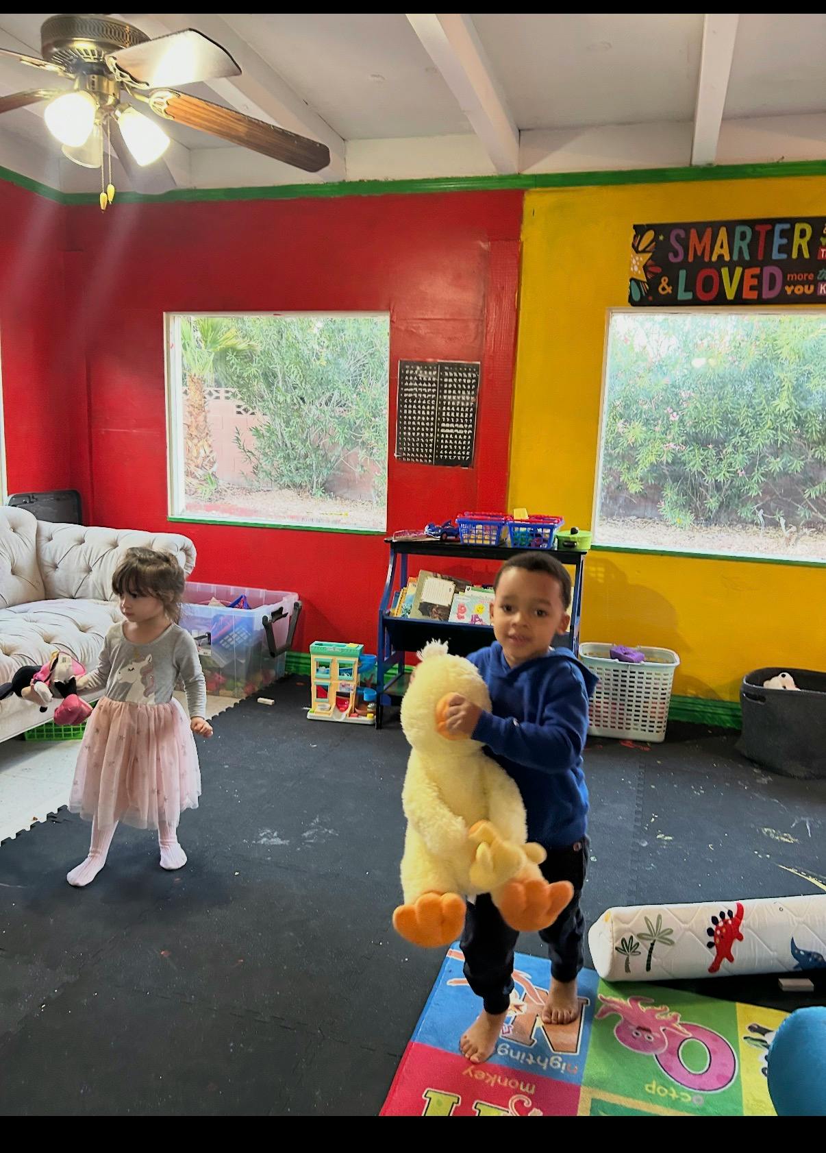 Two children playing indoors, one holding a large yellow stuffed animal