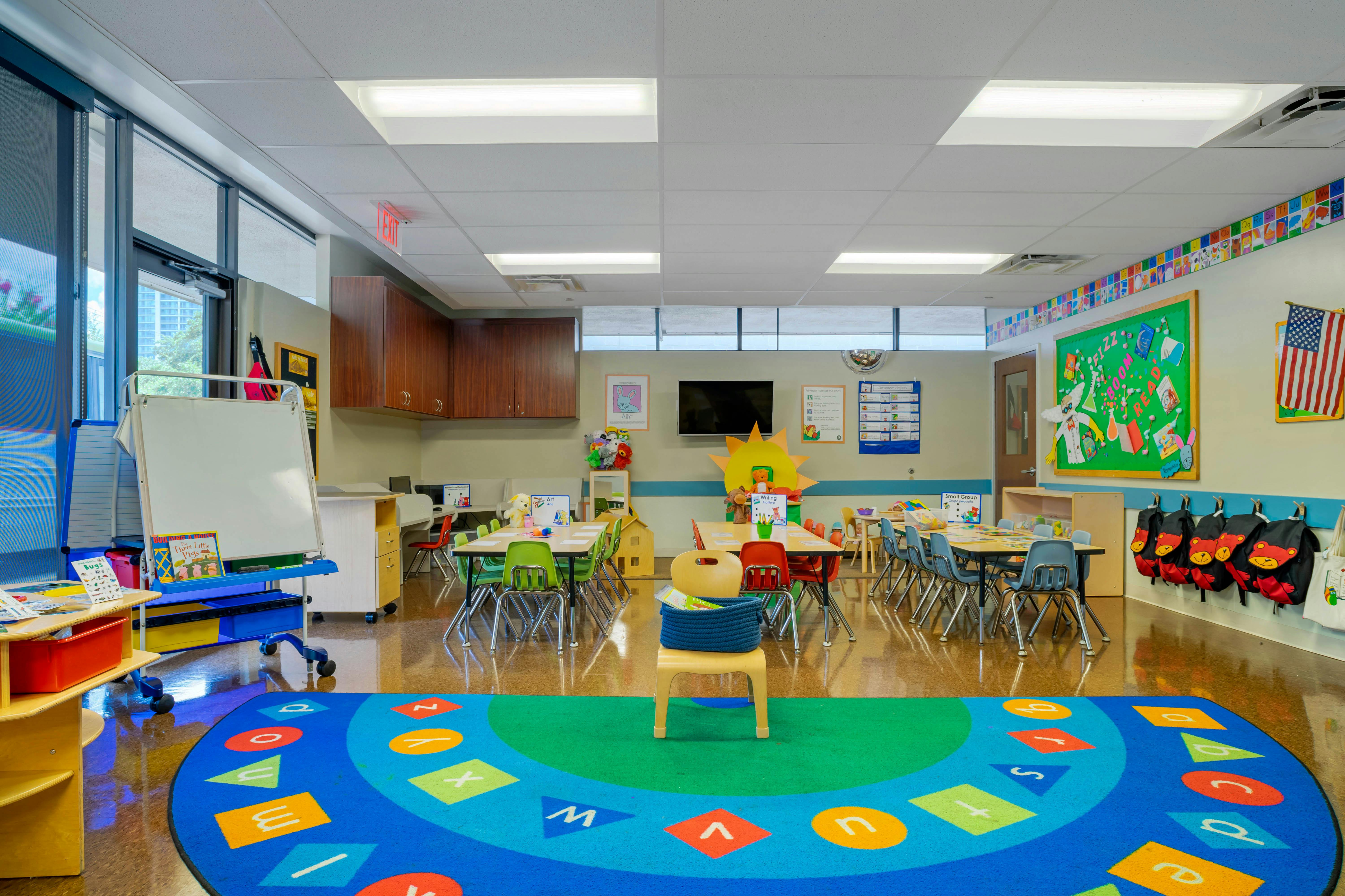 Classroom with small tables and chairs, a colorful alphabet rug on the floor