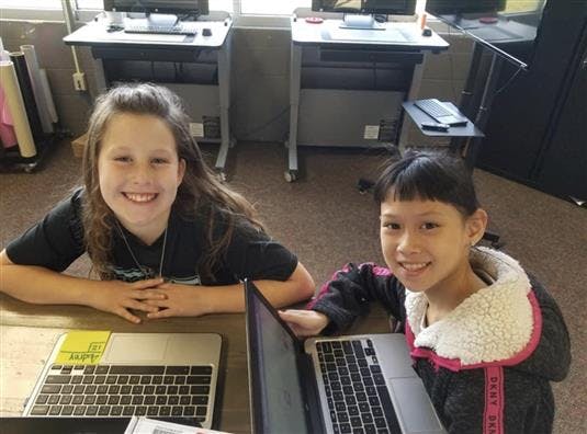 Two children smiling while sitting at laptops in a classroom
