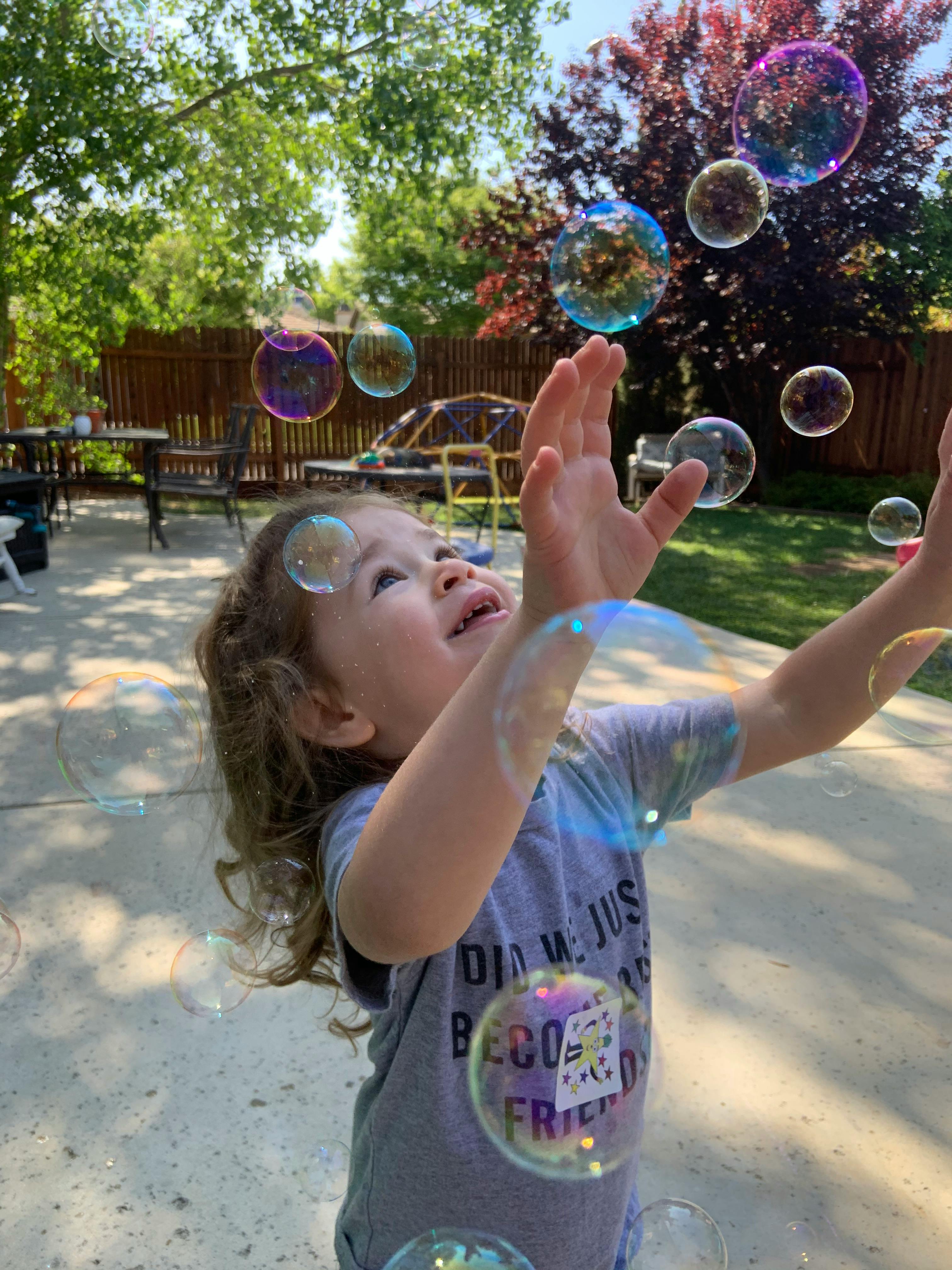 Child reaching up at bubbles outdoors