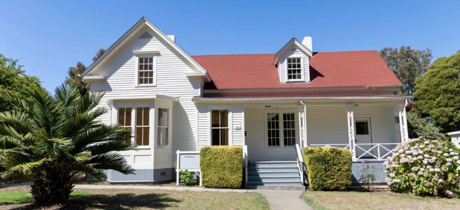 White two-story house with a red roof, a front porch, and steps