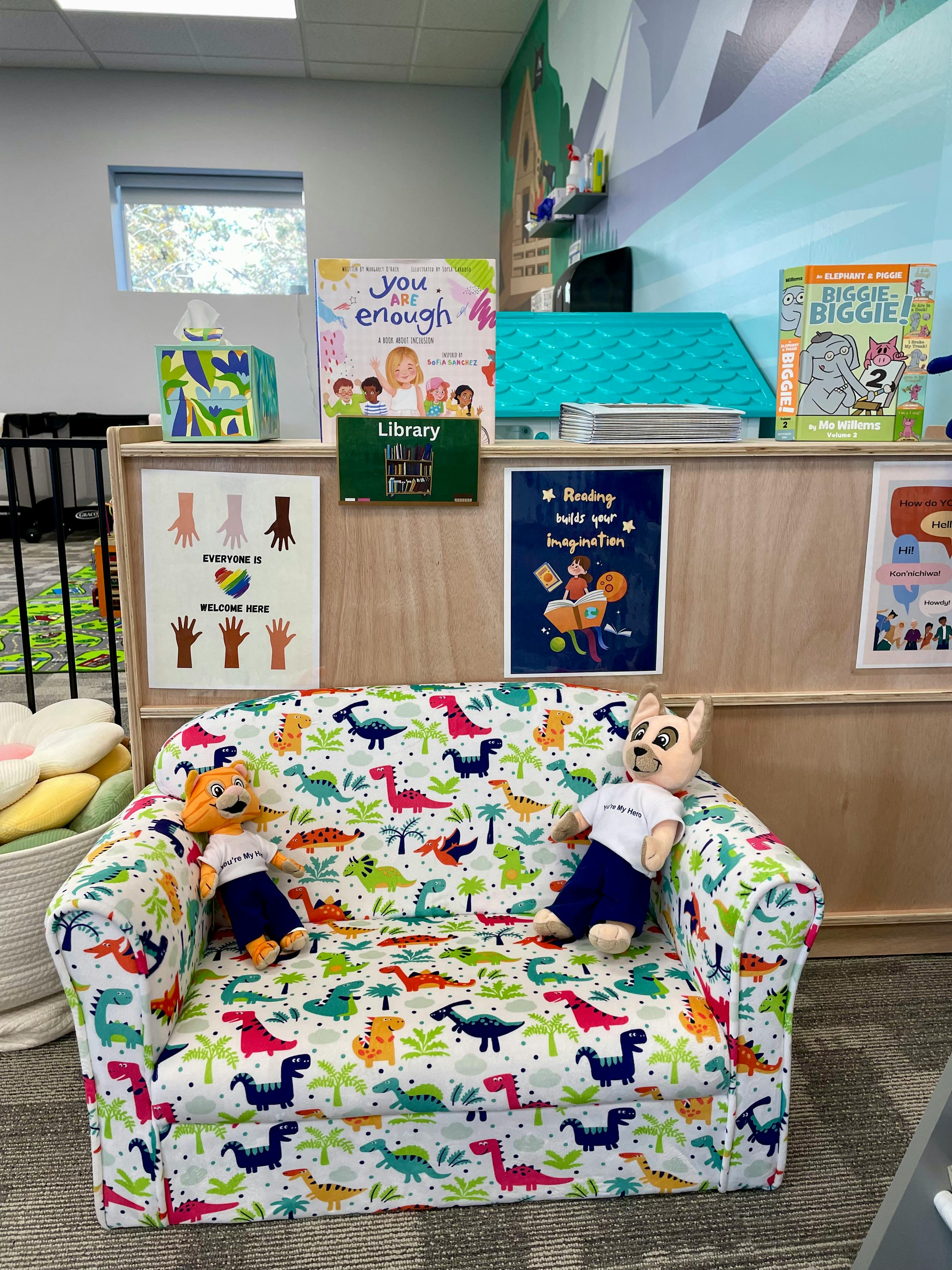 Dinosaur-patterned couch with two stuffed animals in a children's area