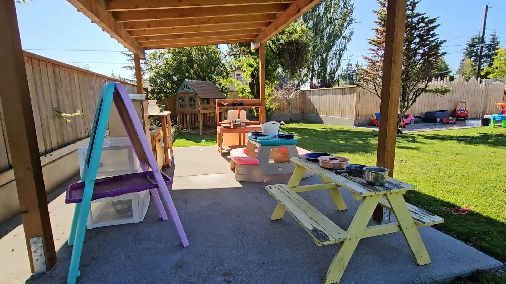 Outdoor play area with a wooden pergola, easel, and picnic table