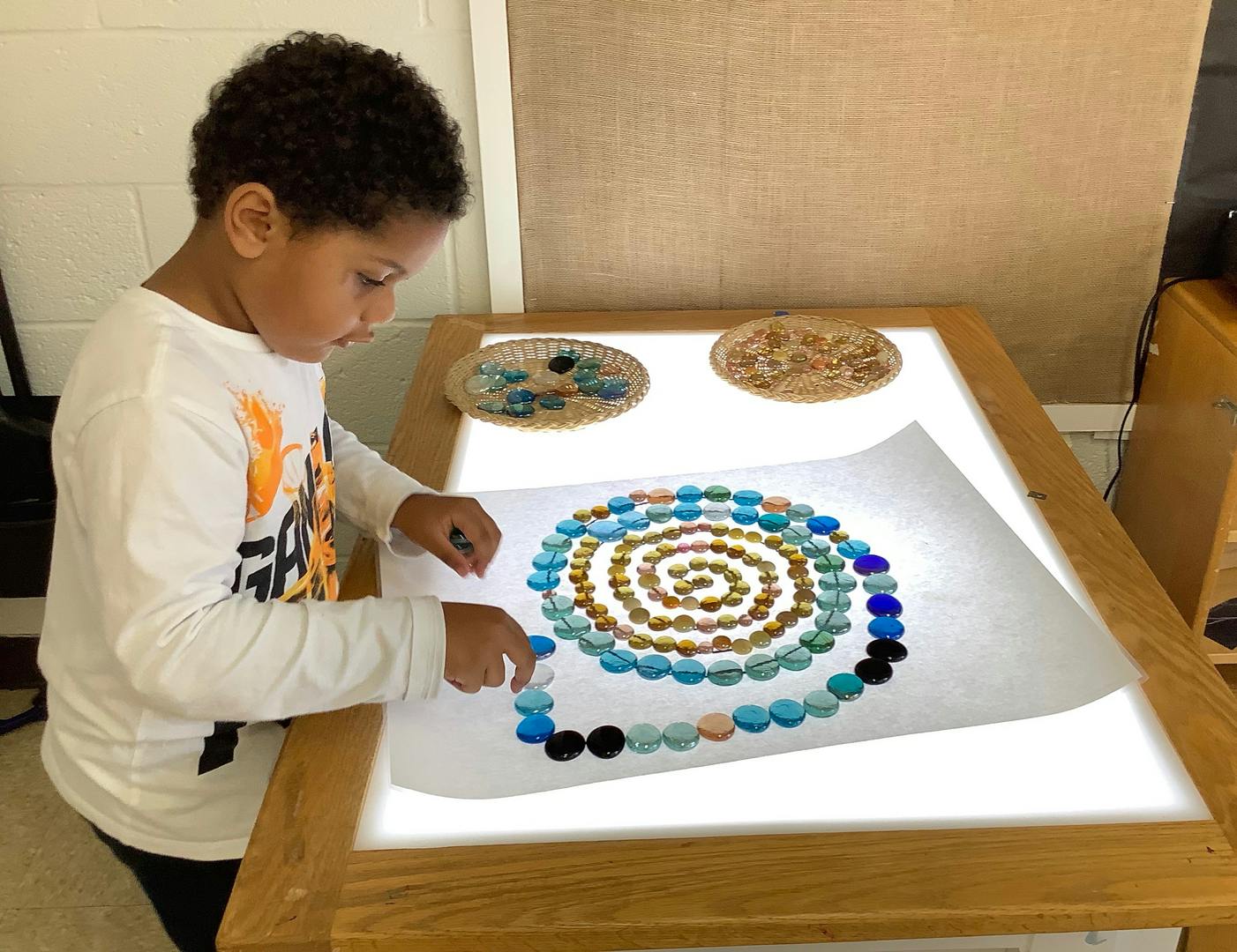 Child arranging colorful beads in a spiral pattern on a light table