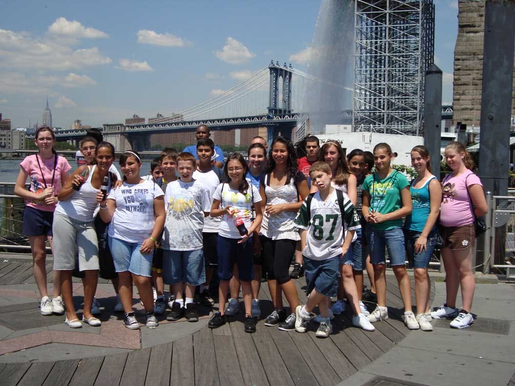 Group of teens and adults standing outdoors with a bridge in the background