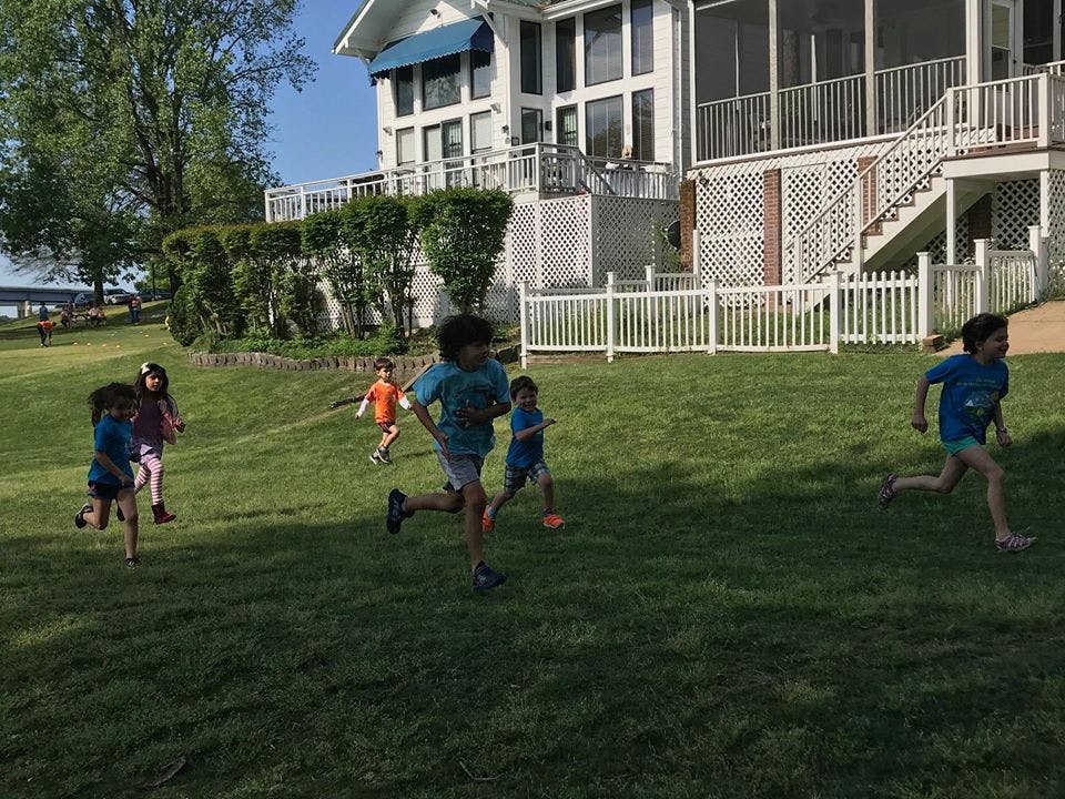 Children running on a grassy lawn in front of a large house