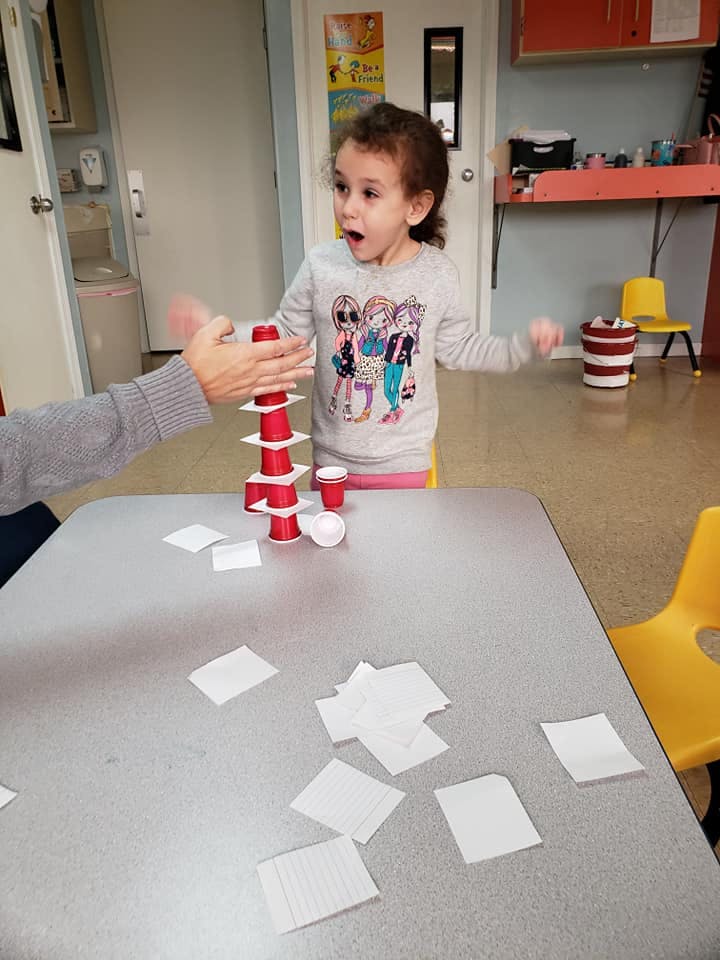 Child and person playing with red cups and white squares on a table