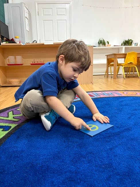 Child on a blue rug pointing at a card with a peace sign