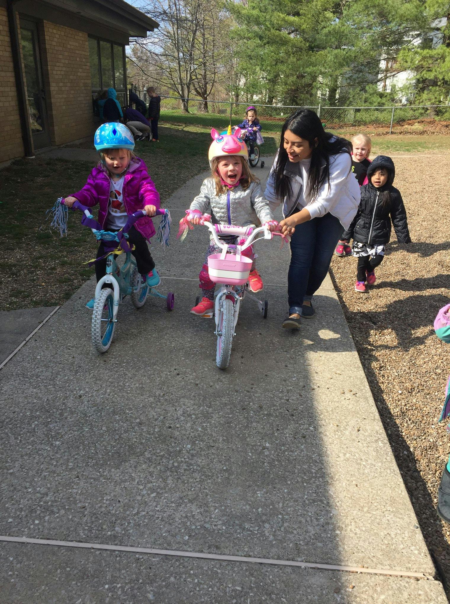 Adult helping a child on a bicycle, another child on a bicycle nearby