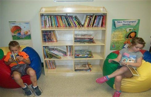 Two children sitting on beanbags reading books in a classroom