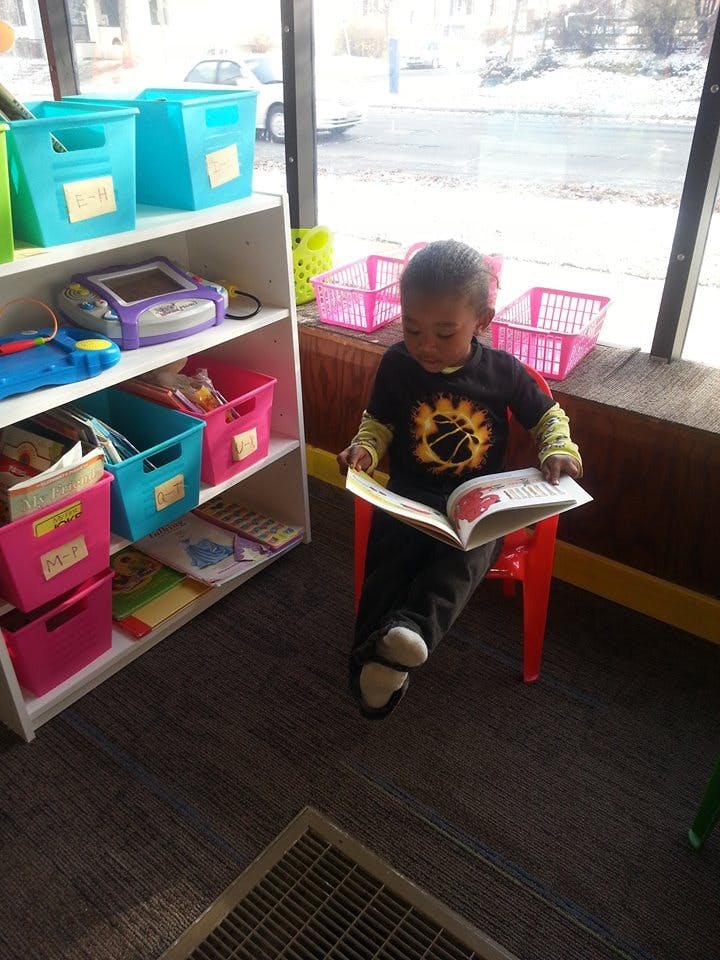 Child sitting on a red chair reading a book