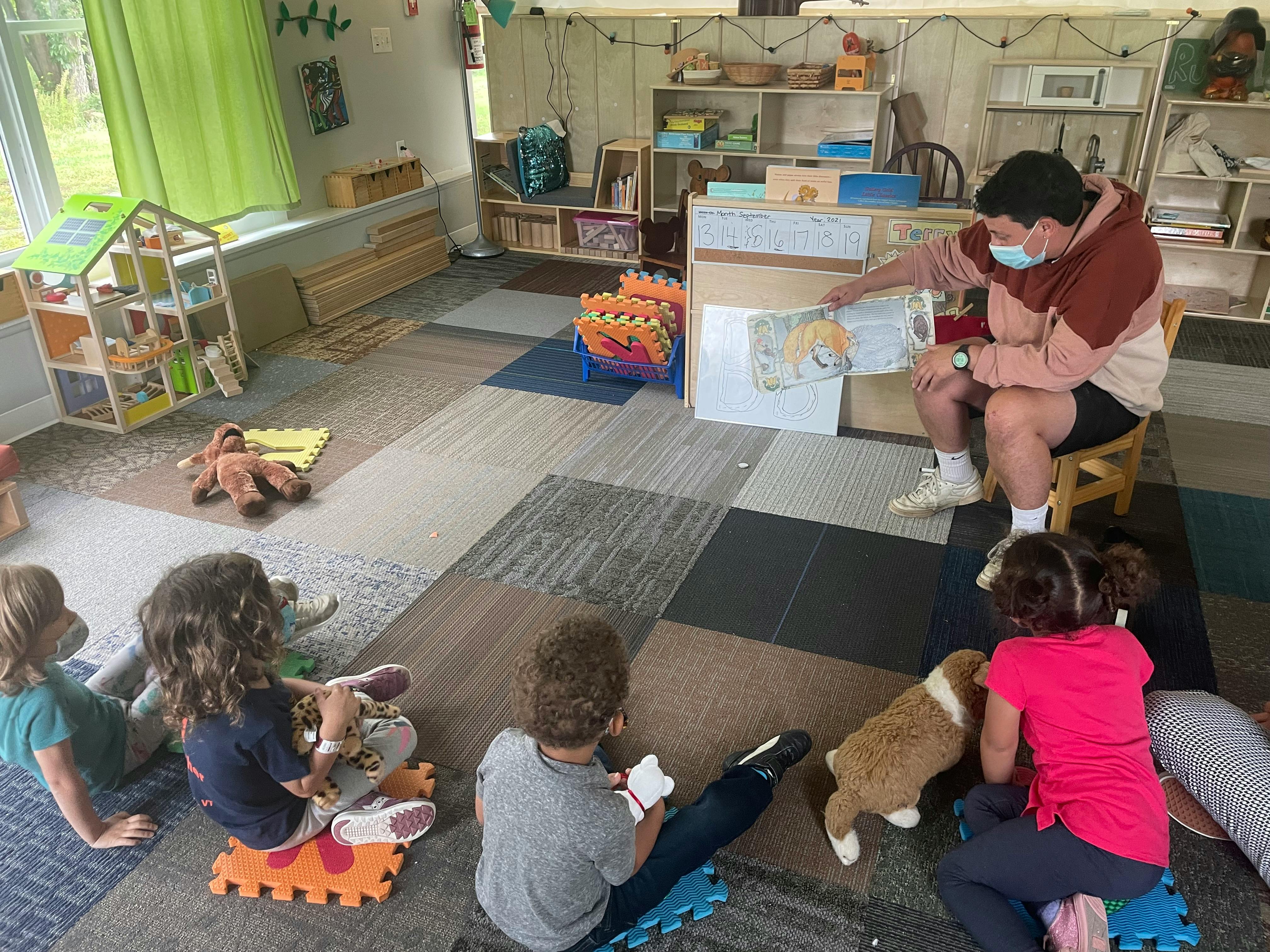 Person in mask reading to children and a dog in a classroom
