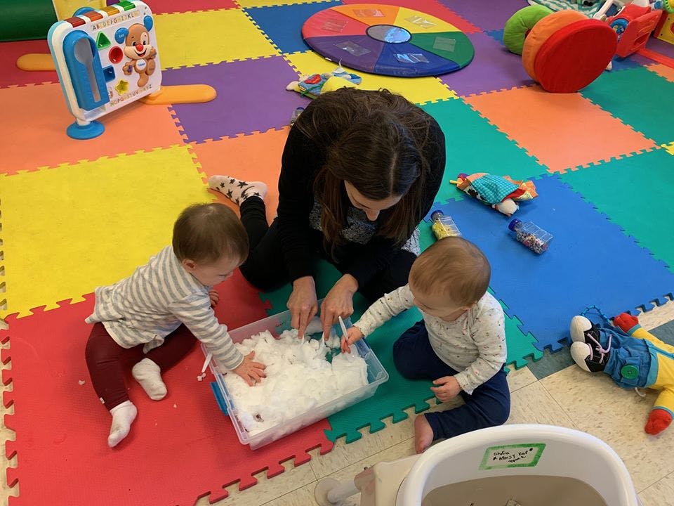Person and two children playing with sensory bin in a classroom