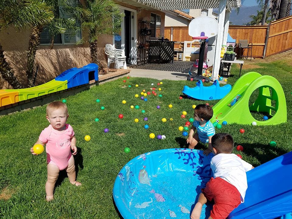 Three children playing with colorful balls and toys in a grassy yard