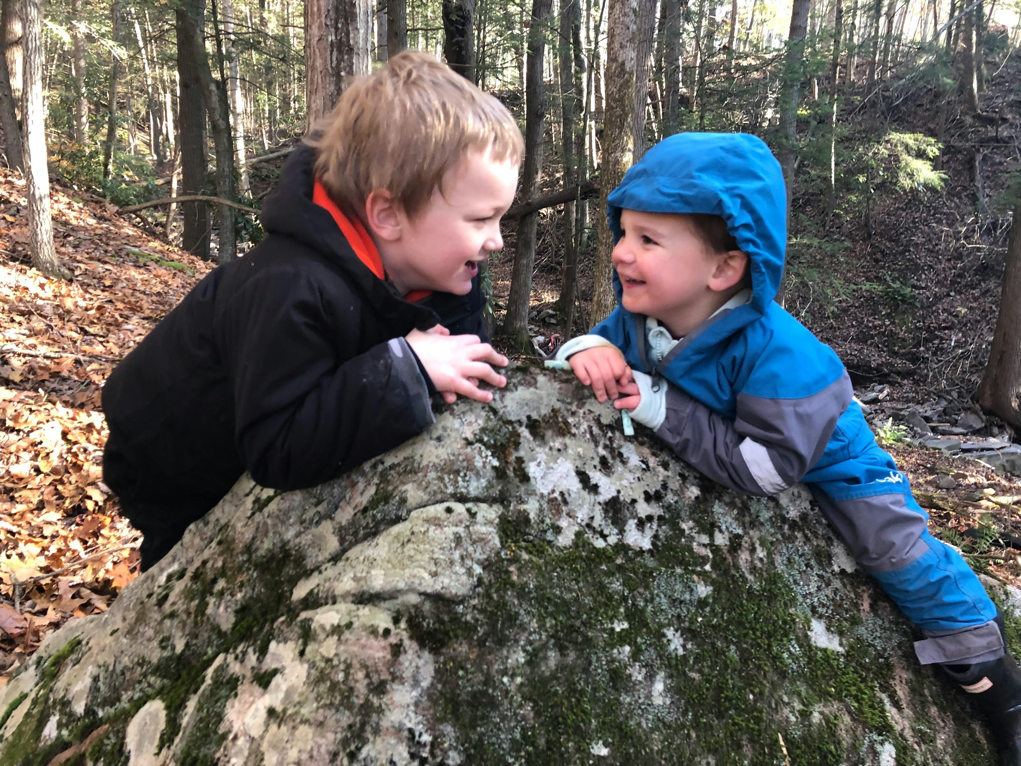 Two children looking at each other over a mossy rock in a forest