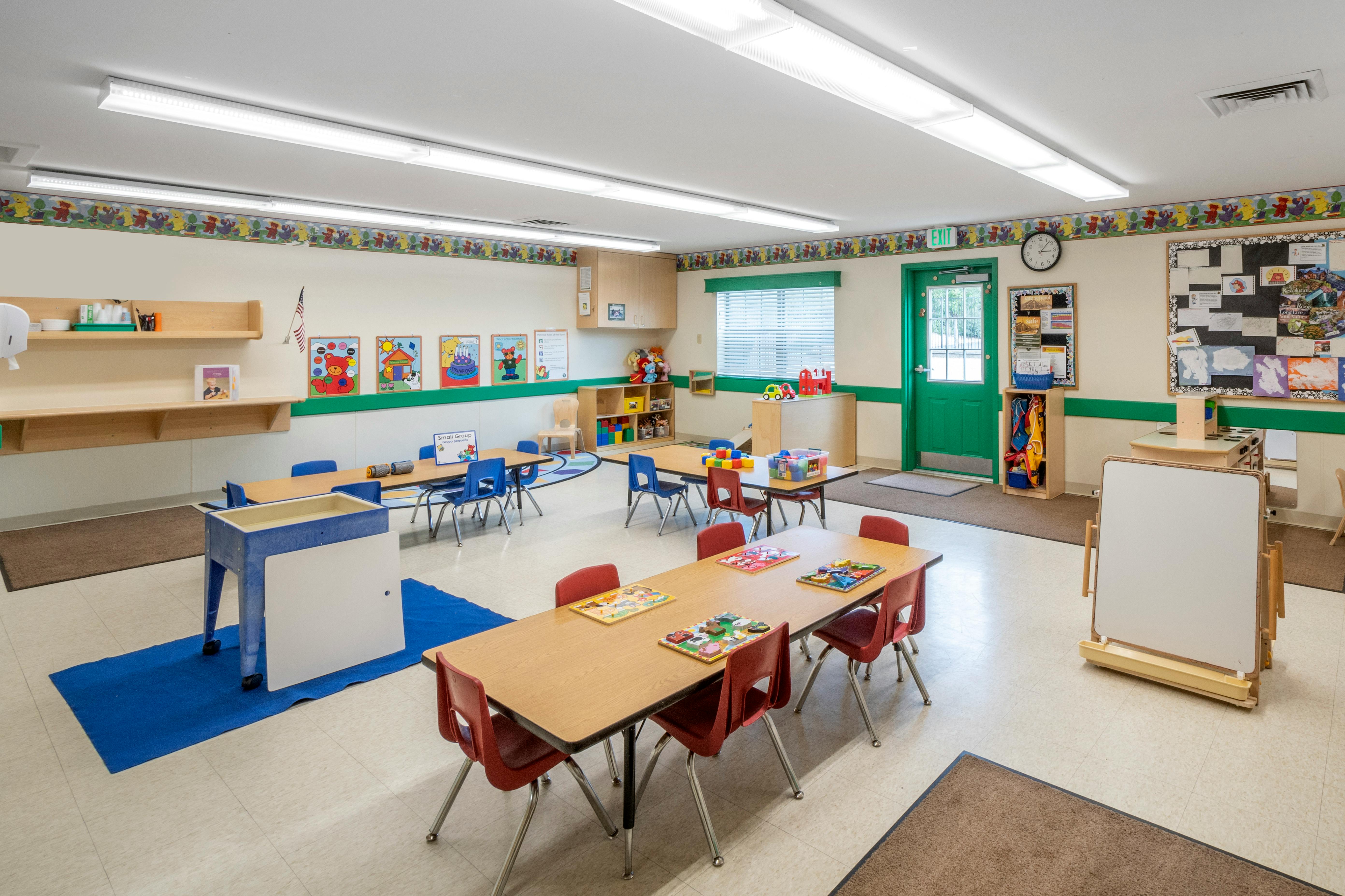 Empty classroom with small tables and chairs, toys, and educational posters