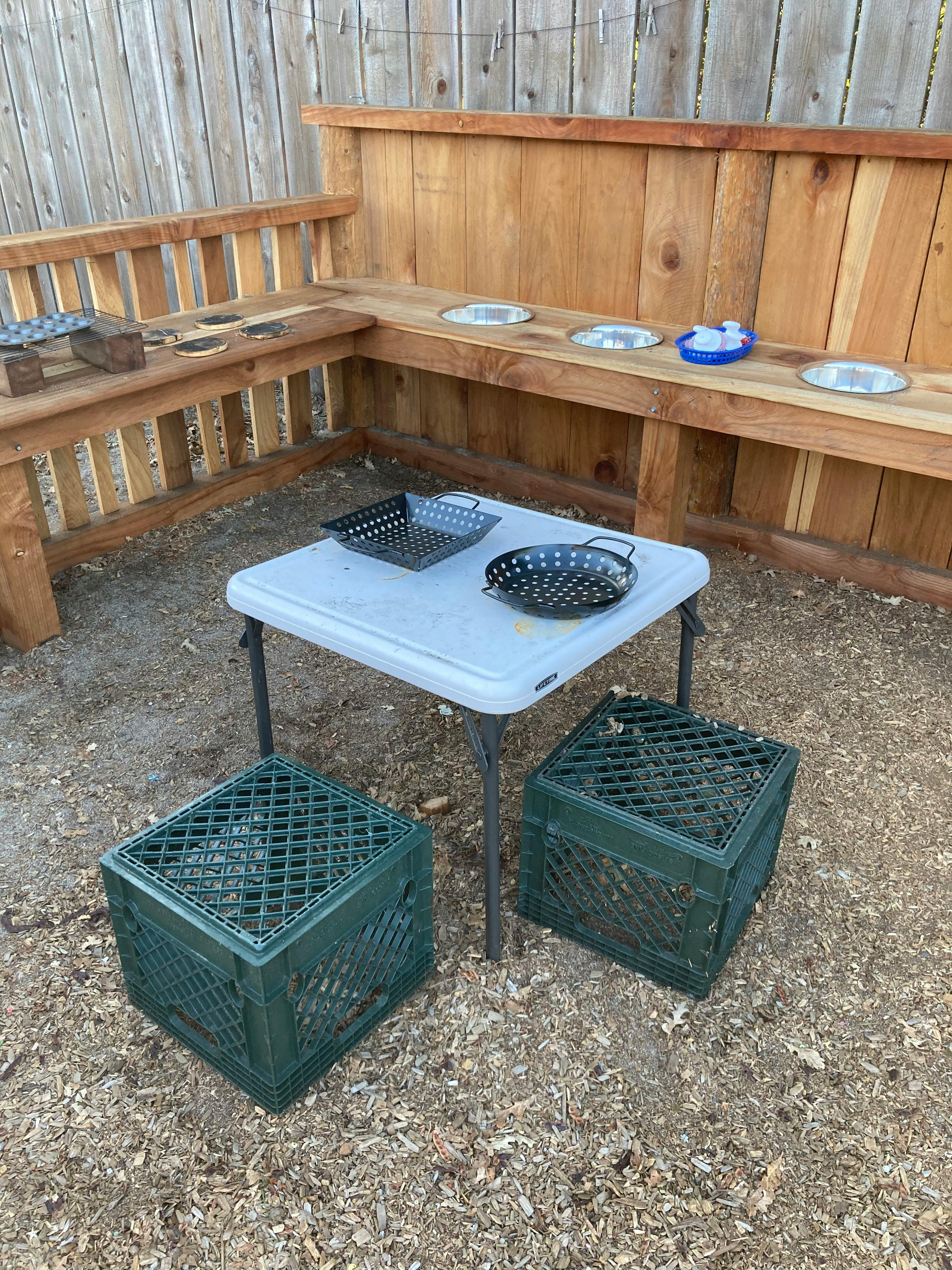 Outdoor play area with a small table, two crates, and wooden benches